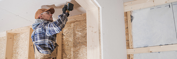 Contractor wears safety equipment as he drills into the ceiling of a home under construction.